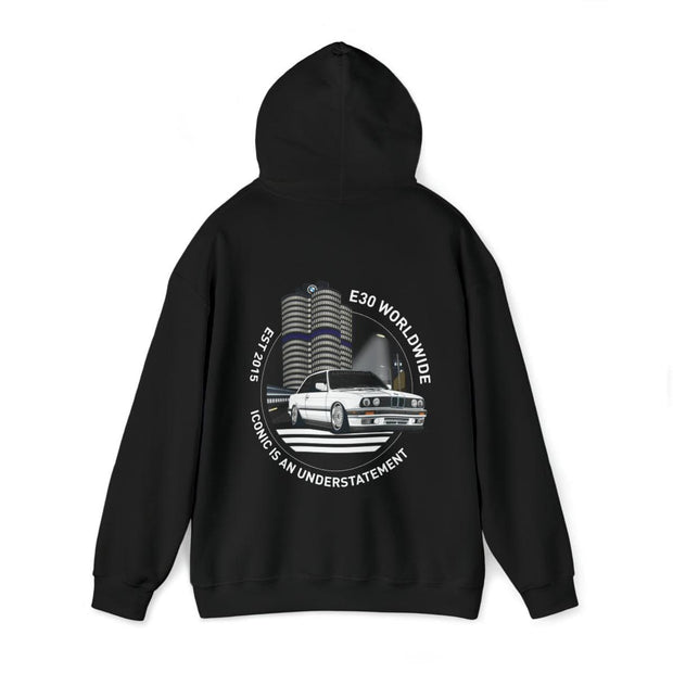 Black hoodie featuring a white classic car illustration with 'E30 WORLDWIDE' text above and 'ICONIC IS AN UNDERSTATEMENT' below, set against a stylized representation of Munich's iconic towers.